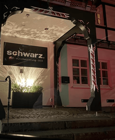 Eingangsbereich von schwarz. bei Nacht mit beleuchtetem Firmenschild